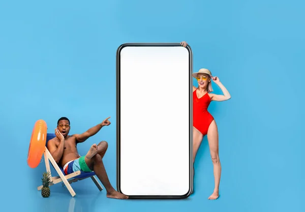 Happy Excited Multienthic Couple Wearing Swimsuits Relaxing Near Big Blank Smartphone — Stockfoto