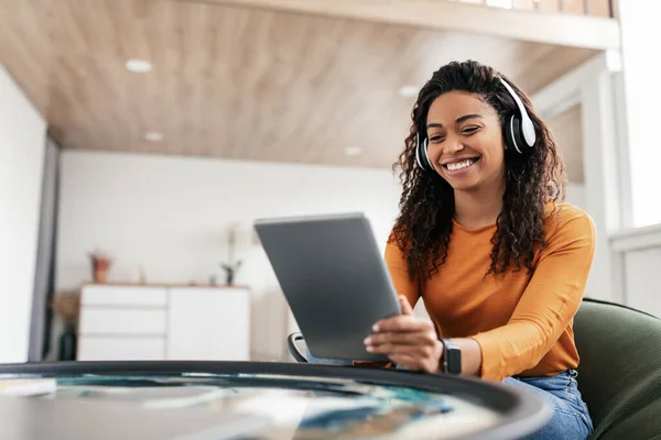 Smiling black woman in headset using tablet in living room