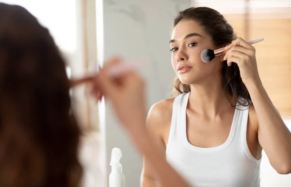 Молодая женщина делает макияж, нанося порошок для лица кистью в помещении — стоковое фото