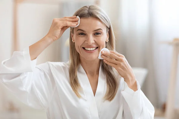 Happy middle aged woman removing make up, using cotton pads — Stockfoto