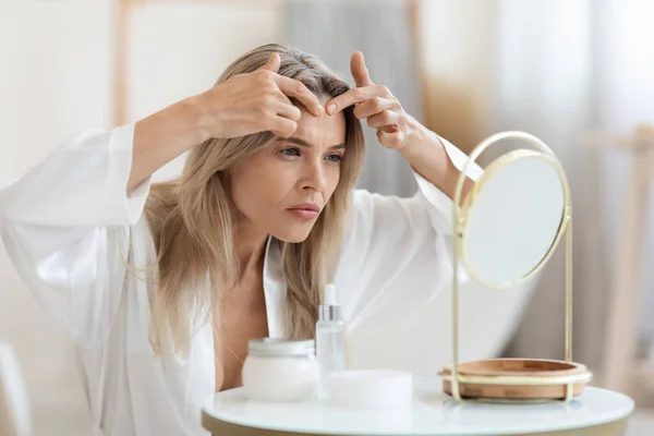 Middle-aged lady sitting in front of mirror, removing blackheads — Stok fotoğraf