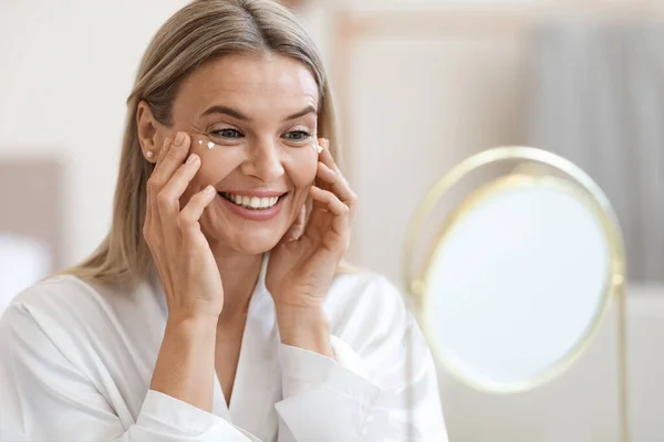 Happy beautiful adult lady using moisturizing eye cream — Stock Fotó