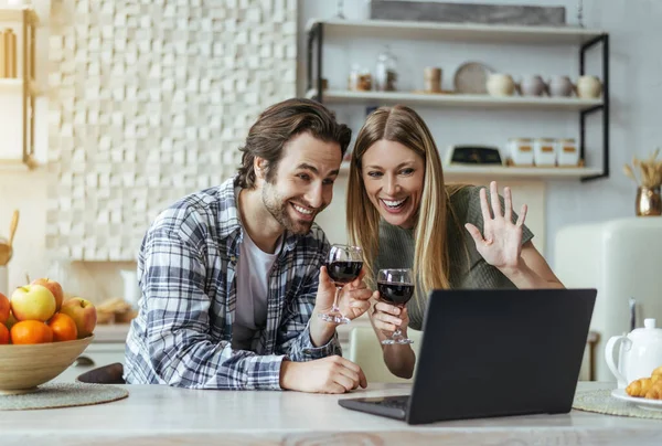Happy surprised european millennial man with stubble and blonde lady with glasses of wine waving hand at laptop webcam — Stok fotoğraf