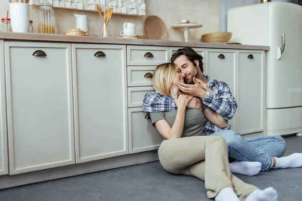 Smiling happy european millennial man with stubble and blonde wife enjoy tender moment, hugging, sitting on floor — 스톡 사진