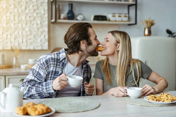 Glad european millennial couple eating cookies and drinking coffee, have breakfast in light kitchen — Stock fotografie