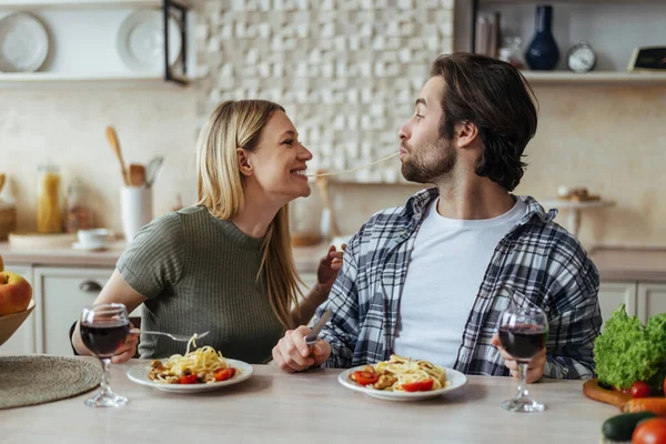 Glad happy handsome caucasian millennial couple eat pasta together, have fun in light kitchen interior, profile — Stock fotografie