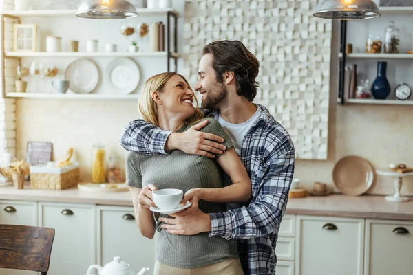 Smiling caucasian millennial male with stubble hugs blonde female, drink coffee, enjoy tender moment — 스톡 사진