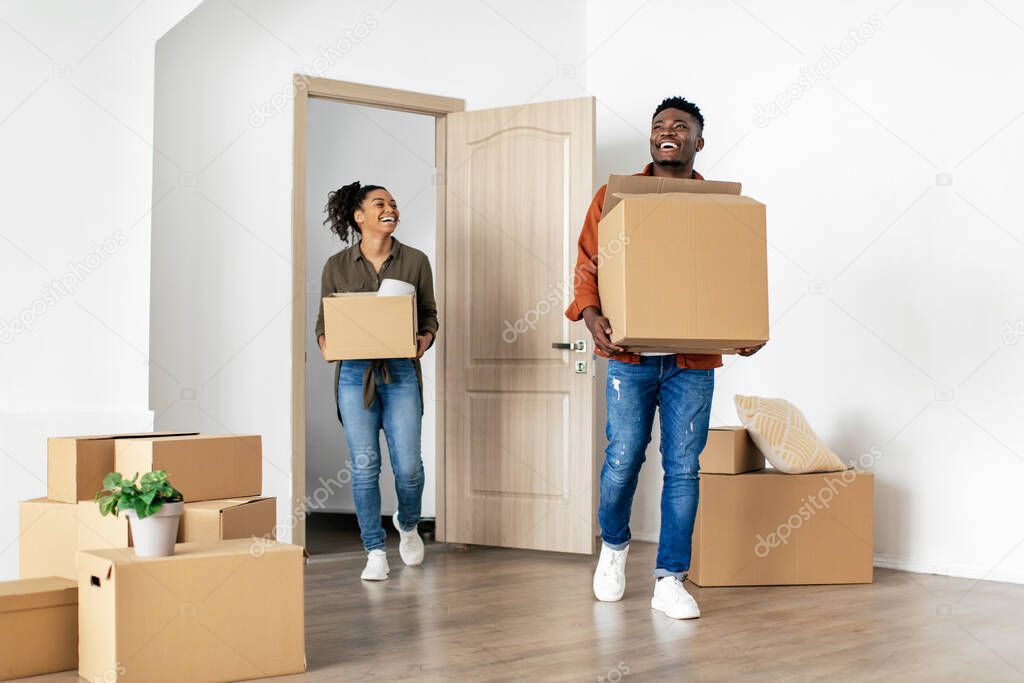 Joyful African American Couple Coming Into House Carrying Moving Boxes