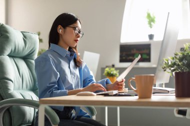 Elinde kağıt okuma raporu tutan bir kadın evde dizüstü bilgisayarla çalışıyor.