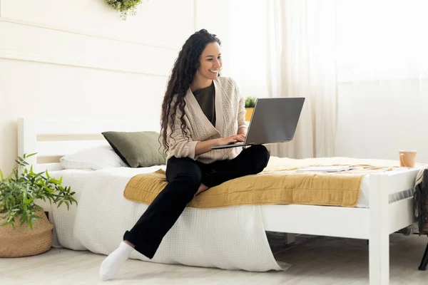 Leende kvinna som använder laptop sittandes på sängen hemma — Stockfoto