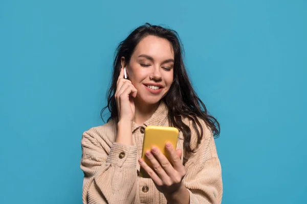 Happy young european brunette female with wireless headphones look at smartphone — Foto de Stock