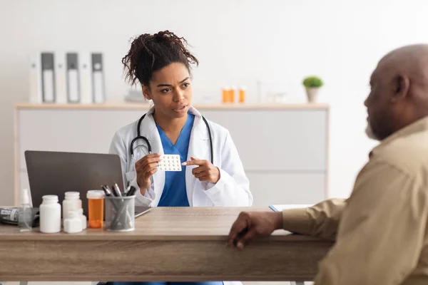Kobieta czarny lekarz pokazuje pigułki dla pacjenta płci męskiej — Zdjęcie stockowe