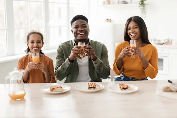 Familia africana sosteniendo vasos bebiendo jugo de naranja fresco en la cocina — Foto de Stock