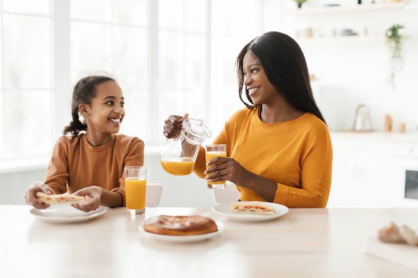 Afrika kökenli Amerikalı anne ve kızı mutfakta portakal suyu içiyor. — Stok fotoğraf