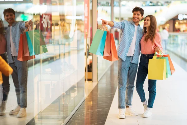 Alışveriş merkezinin vitrininde parmak gösteren bir çift.