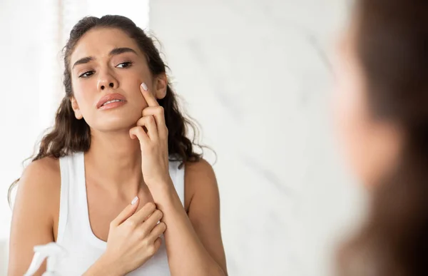 Depressed Woman Touching Pimple On Face In Modern Bathroom — стоковое фото