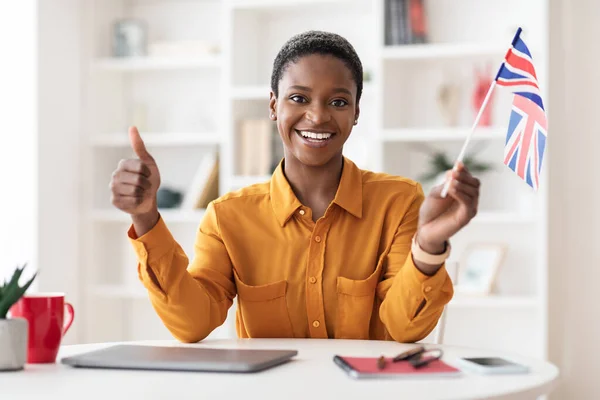 Cheerful black woman holding flag of UK, showing thumb up — стоковое фото