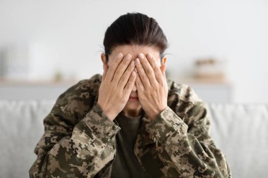 Askeri üniformalı, elleri ile yüzünü kapatan depresif kadın portresi.