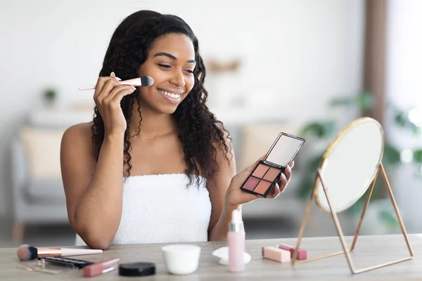Hermosa mujer negra sosteniendo la paleta de contorno, poniendo maquillaje — Foto de Stock