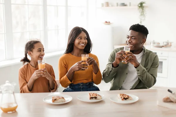 Familia negra bebiendo jugo de naranja disfrutando del desayuno sentado en la cocina — Foto de Stock