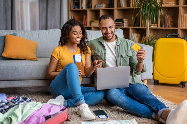 Excited black spouses using laptop and booking hotel online with credit card, sitting with suitcases on floor at home — Φωτογραφία Αρχείου
