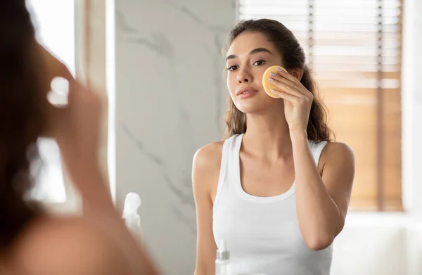 Привлекательная леди с помощью косметической губки делает макияж стоя в ванной комнате — стоковое фото