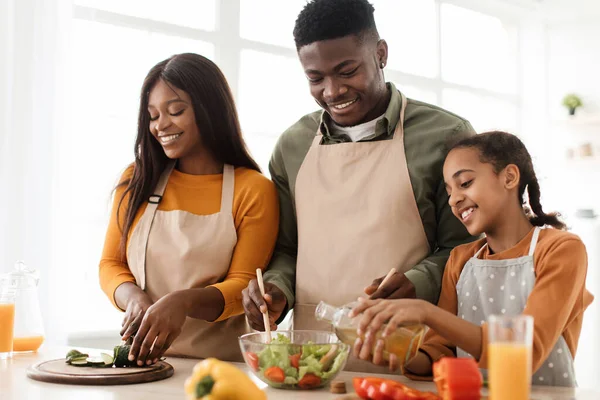 Familia afroamericana de tres cocineros haciendo ensalada en la cocina — Foto de Stock