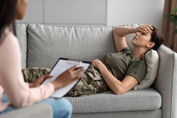 TEPT. Mulher militar deprimida deitada no sofá durante sessão de terapia com psicólogo — Fotografia de Stock
