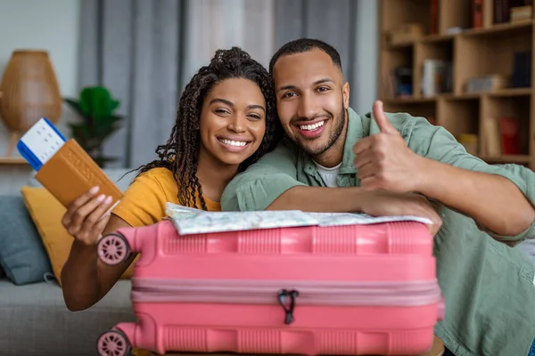 Vacation concept. Excited african american spouses holding passports and showing thumb up, leaning on suitcase —  Fotos de Stock