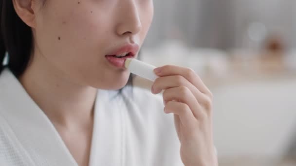 Nahaufnahme Porträt einer Frau, die hygienischen Lippenstift auf die Lippen aufträgt, sich selbst im verschwommenen Badezimmer befeuchtet, leeren Raum — Stockvideo