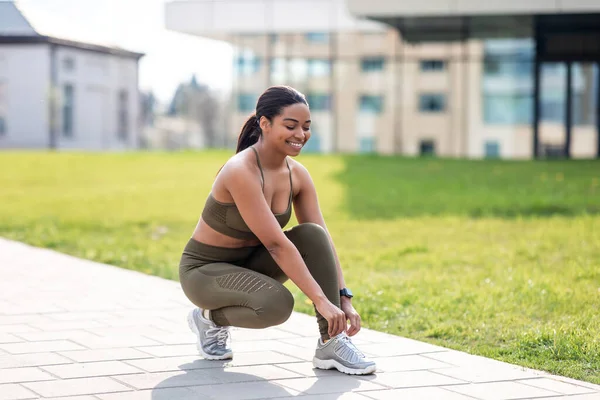 Joyeux jeune femme afro-américaine attachant des lacets sur ses baskets avant l'entraînement, jogging au parc de la ville, espace vide — Photo