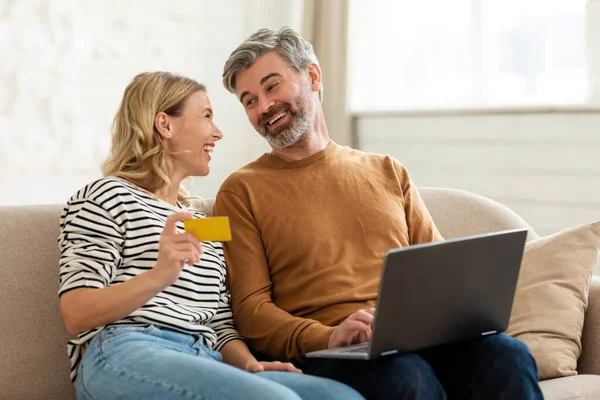 Pareja feliz compras en línea usando el ordenador portátil y la tarjeta de crédito en interiores —  Fotos de Stock