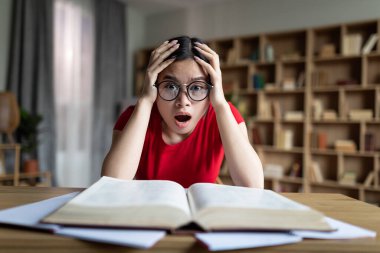 Gözlüklü, ağzı açık, kafası masada, elleri kitapla dolu, korkmuş genç Japon kız öğrenci.