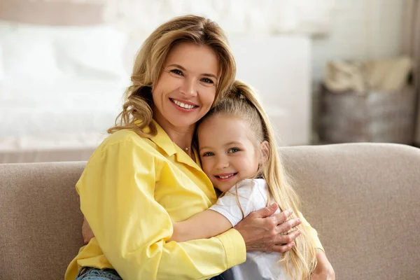 Glad mamma och lilla dotter omfamnande leende till kameran inomhus — Stockfoto