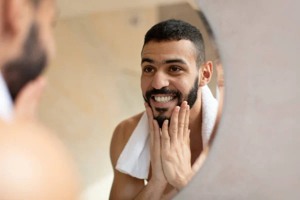 Joven árabe confiado mirándose en el espejo, tocando la barba — Foto de Stock