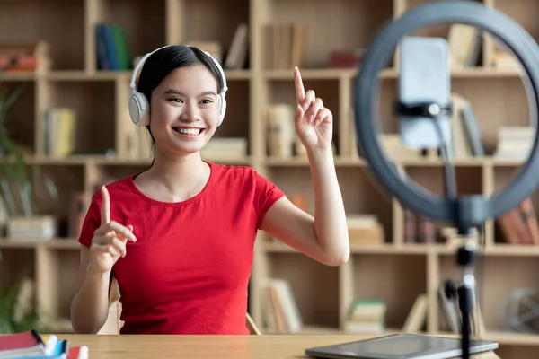 Feliz joven asiática mujer en los auriculares inalámbricos gesto con las manos y mirar el teléfono inteligente webcam —  Fotos de Stock