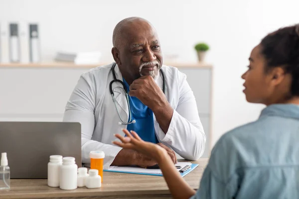 Зрелый чёрный врач слушает молодую пациентку — стоковое фото