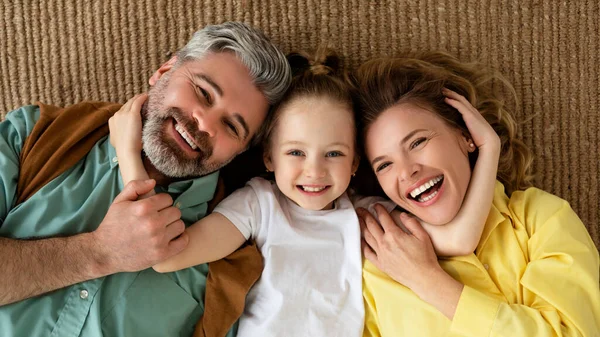 Genitori gioiosi e figlia che abbracciano sdraiati sul pavimento a casa — Foto Stock