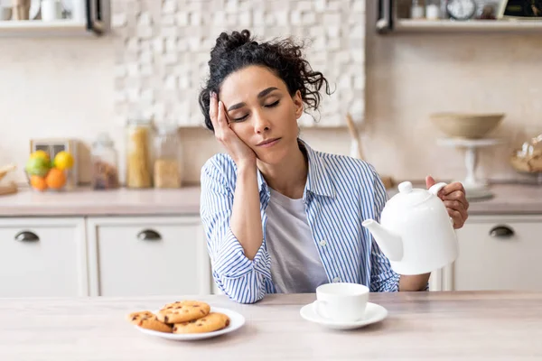 寝たきりの若い女性がカップにお茶を注ぎ、眠って、早起きし、キッチンのインテリアのテーブルに座って、フリースペース — ストック写真
