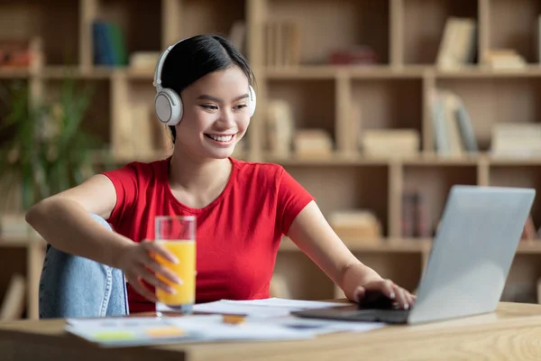 Mujer coreana joven feliz en auriculares inalámbricos estudiando con el ordenador portátil en el interior de la sala de estar —  Fotos de Stock