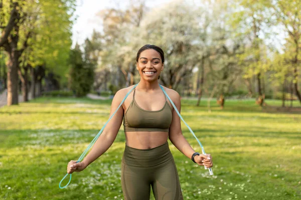 Felice giovane donna nera in abbigliamento sportivo in posa con corda di salto al parco della città — Foto Stock