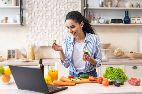Mujer latina feliz cocinando la cena y las videollamadas en el portátil, hablando con la cámara web, de pie en la cocina en su apartamento — Foto de Stock
