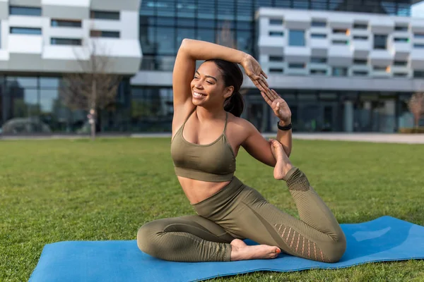 Mujer negra joven flexible haciendo postura de paloma de yoga durante la práctica al aire libre en el parque de la ciudad, espacio de copia —  Fotos de Stock