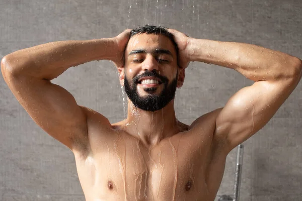 Handsome happy young Arabic male model enjoying taking hot shower