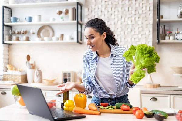 Nützliches Kochen und Foodblog. Positive Frau macht frischen Salat, blickt auf Laptop und gestikuliert, Kücheneinrichtung — Stockfoto