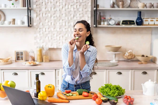 Mujer latina joven cocinando ensalada de verduras frescas y pepino mordedor, preparando el almuerzo en casa en la cocina —  Fotos de Stock