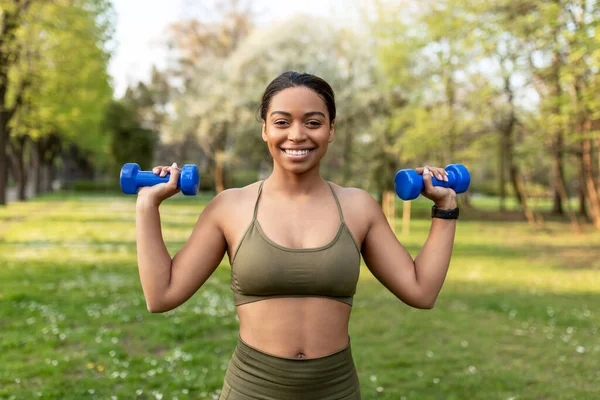 Concepto de entrenamiento de fuerza. Ajuste joven mujer negra haciendo ejercicios con mancuernas en el parque de la ciudad — Foto de Stock