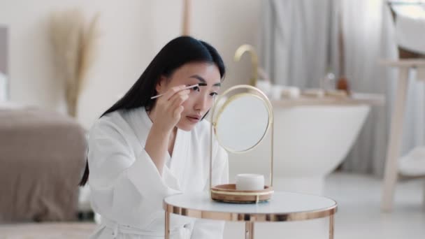 Ochtend goedmaken. Jonge mooie aziatische vrouw van toepassing speciale mascara voor wenkbrauwen, voor te bereiden op het uitgaan — Stockvideo