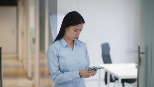 Joven mujer de negocios asiática confiada contando pila de billetes de dólar, de pie en la oficina, cámara lenta, espacio libre — Vídeos de Stock