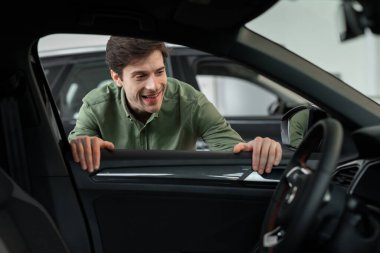 Yakışıklı genç adam yeni arabanın penceresinden bakıyor, modern mağazadan almadan önce kontrol ediyor.